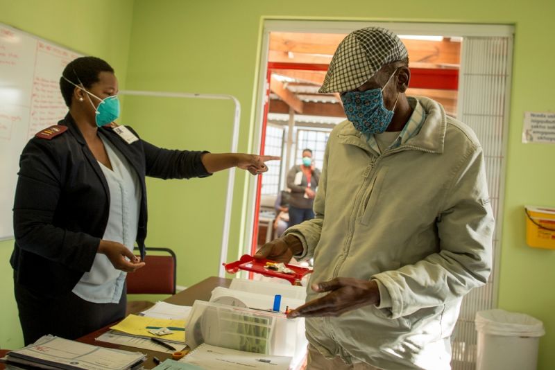 A woman and a man wearing medical masks are standing working with papers and small items.